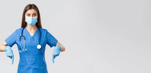 Covid-19，防止病毒、健康、保健工作者和检疫概念。有决心的女护士或医生，身穿蓝色的刷子，戴着医疗面罩和手套，手指朝下，展示信息横幅 — 图库照片