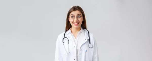 Healthcare workers, medicine, insurance and covid-19 pandemic concept. Happy optimistic female doctor, physician with stethoscope in white scrubs and glasses, look upper left corner with upbeat smile — Stock Photo, Image