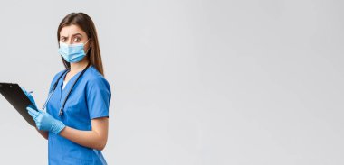 Covid-19, virüsün önlenmesi, sağlık, sağlık çalışanları ve karantina konsepti. Şüpheci ve şüpheci bayan hemşire, mavi önlüklü doktor hasta formlarını doldurup panoda kamerayı şaşırttı.