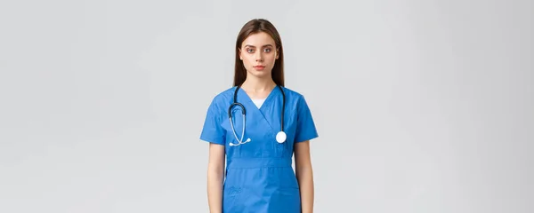 Travailleurs de la santé, prévenir le virus, concept d'assurance et de médecine. Jeune infirmière au look sérieux, médecin en blouse bleue et stéthoscope, regardant la caméra, debout fond gris — Photo