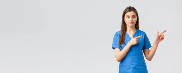 Медицинские работники, предотвратить вирус, страхование и медицина концепции. Молодая медсестра или врач в синей форме, указывая пальцами право, рекомендую баннер или промо для пациентов клиники — стоковое фото