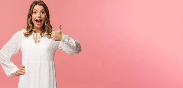 Buena idea. Upbeat, entusiasta chica rubia caucásica en vestido blanco de primavera, escuchar un buen plan, mostrar los pulgares hacia arriba y asentir con la cabeza en la aprobación, de acuerdo y recomendar, satisfecho con la opción, de pie fondo rosa — Foto de Stock