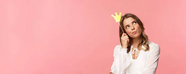 Concepto de primavera, felicidad y celebración. Retrato de cerca de la joven niña confiada y atractiva reflexiva sintiéndose como la reina de la fiesta nocturna, soñando despierto, pensando con máscara de corona en la cabeza — Foto de Stock