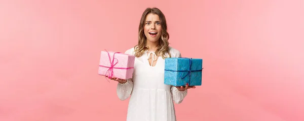 Fiestas, celebración y concepto de mujer. Retrato de chica rubia sorprendida e impresionada no esperaba recibir tantos regalos, sosteniendo dos regalos envueltos y una cámara sonriente asombrada — Foto de Stock