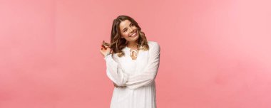 Feminen, güzel ve seksi sarışın bir kadın şık beyaz sping elbiseler giymiş, kıkırdayıp sağa bakıyor, kıvırcık saçlarıyla pembe arka planda biriyle flört ediyor.