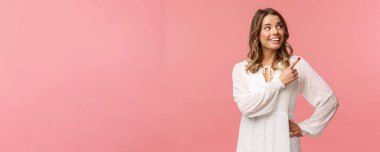 Şuna bir bak. Hoş, güzel, sarışın, Avrupalı, 20 'li yaşlarda, beyaz, şirin elbiseli, sağ üst köşesini işaret eden, gülümseyen, memnun, iyi bir tekliften memnun, pembe arka planı olan bir kadın.