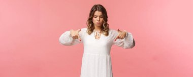 Kasvetli, kıskanç ve üzgün, beyaz modaya uygun bahar elbisesi giymiş, yüzü asık, pahalı bir şey görüyor, pembe arka planda yaşayamıyor.