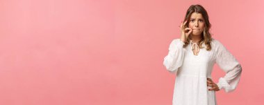 Endişeli sarışın kız kimseye söylemeyeceğine söz ver, hızlı dudaklı jest yap, endişeli ol, gizli birini duy, durum hakkında sessiz kal, pembe arka planda utangaç dur.