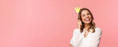 Bahar, mutluluk ve kutlama konsepti. Çekici gülümseyen, güzel sarışın kızın yakın plan portresi, küçük kraliçe tacı tutan, neşeyle gülen, güçlü ve mutlu, pembe arka plan