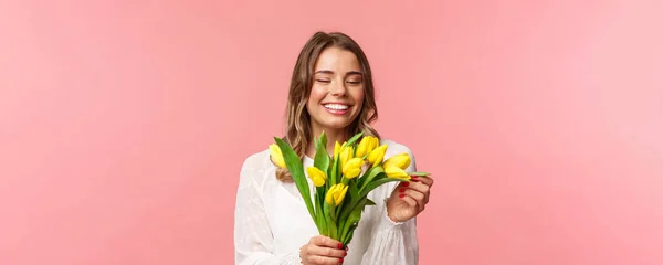 Bahar, mutluluk ve kutlama konsepti. Sarı lale yaprağına dokunan, elinde çiçekler tutan, randevuda buket alan pembe arka planda duran sevimli, romantik kızın yakın plan portresi. — Stok fotoğraf