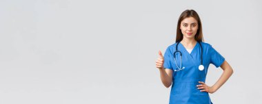 Tıp çalışanları, covid-19 ve aşı konsepti. Kendine güvenen profesyonel doktor, mavi önlüklü ve steteskoplu bayan hemşire, baş parmaklarınızı kaldırın, klinikteki en iyi hizmeti sağlayın veya garanti edin.