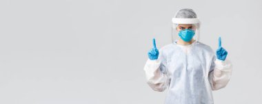 Covid-19, virüsün önlenmesi, sağlık, sağlık çalışanları ve karantina konsepti. Hasta Coronavirüs hastalarıyla çalışan kararlı genç bir doktor ya da hemşire. Parmakla işaret ediyor, koruyucu elbise giyiyor.