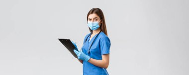 Covid-19, virüsün önlenmesi, sağlık, sağlık çalışanları ve karantina konsepti. Şüpheci ve şüpheci bayan hemşire, mavi önlüklü doktor hasta formlarını doldurup panoda kamerayı şaşırttı.
