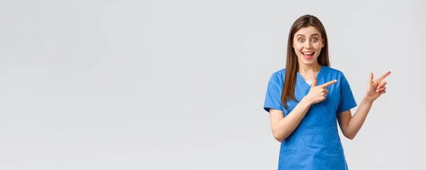 Медицинские работники, предотвратить вирус, страхование и медицина концепции. Взволнованная счастливая медсестра или доктор в синем халате, указывающая пальцем направо, выглядящая забавной, сообщающая о промо или хороших новостях — стоковое фото