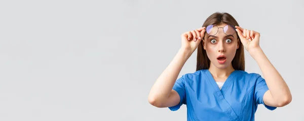 Trabajadores sanitarios, medicina, seguros y concepto de pandemia covid-19. Enfermera sorprendida o sorprendida, doctora en uniformes azules, boca abierta y gafas de despegue asombrada — Foto de Stock