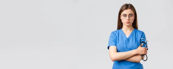 Trabajadores sanitarios, medicina, seguros y concepto de pandemia covid-19. Enfermera profesional, seria y decidida, doctora en uniformes azules, con estetoscopio, gafas, mirada confiada — Foto de Stock