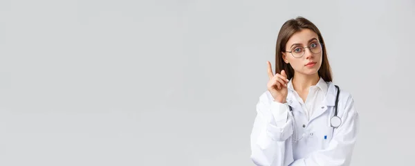 Trabajadores sanitarios, medicina, seguros y concepto de pandemia covid-19. Doctora profesional inteligente en bata blanca y gafas, tener idea, sugerencia, levantar el dedo índice eureka signo — Foto de Stock