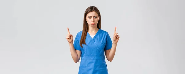 Operatori sanitari, prevenire virus, assicurazione e medicina concetto. Agitato singhiozzando infermiera carina o medico in camice blu, bronza, si sentono a disagio puntando il dito verso l'alto a spiacevoli cattive notizie, mostra banner — Foto Stock