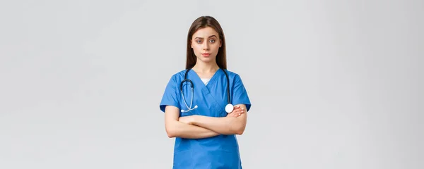 Operatori sanitari, prevenire virus, assicurazione e medicina concetto. Infermiera scettica o medico in camice blu, petto braccia incrociate e fissare con impazienti, disapprovazione sorridente — Foto Stock