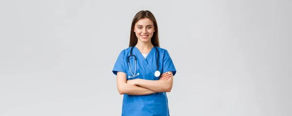 Pracownicy medyczni, opieka zdrowotna, koncepcja covid-19 i szczepień. Optymistyczna, pewna siebie, profesjonalna pielęgniarka lub lekarz w niebieskim fartuchu ze stetoskopem, klatką piersiową krzyżową i uśmiechniętą optymistką — Zdjęcie stockowe
