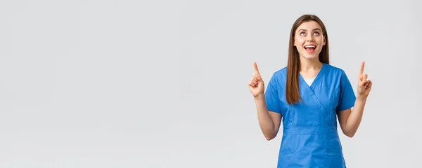 Trabajadores de la salud, prevenir virus, pruebas de detección de covid-19, concepto de medicina. Alegre sonriente bonita doctora o enfermera en uniformes azules, señalando con los dedos hacia arriba y mirando hacia arriba regocijándose — Foto de Stock