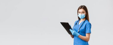 Covid-19, virüsün önlenmesi, sağlık, sağlık çalışanları ve karantina konsepti. Profesyonel kadın hemşire ya da doktor mavi önlüklü, tıbbi maske ve eldivenli hasta bilgilerini not alıyor.
