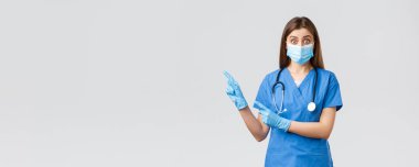 Covid-19, virüsün önlenmesi, sağlık, sağlık çalışanları ve karantina konsepti. İlgili ve sorgulanmış kadın doktor, mavi önlüklü hemşire ve tıbbi maske, solu işaret eden sorular soruyor.