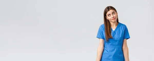 Healthcare workers, prevent virus, insurance and medicine concept. Indecisive and unsure cute doctor, female nurse in blue scrubs, cant tell, have no idea, shrugging and look away uncertain — Stock Photo, Image