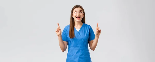 Pracownicy służby zdrowia, zapobiegać wirusom, badania przesiewowe przeciw wirusowi-19, koncepcja medycyny. Wesoły uśmiech ładna kobieta lekarz lub pielęgniarka w niebieskim fartuchu, wskazując palcem w górę i patrząc w górę radując — Zdjęcie stockowe