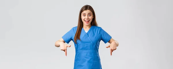 Healthcare workers, prevent virus, covid-19 test screening, medicine concept. Excited happy attractive nurse or doctor in blue scrubs, pointing fingers down, found great promo, showing banner — Stock Photo, Image