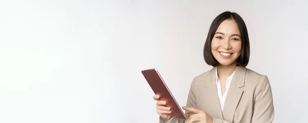 Imagem de empresária asiática, vendedora segurando tablet digital e sorrindo, trabalhando com gadget, de pé em terno sobre fundo branco — Fotografia de Stock