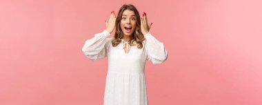 Şaşırmış, mutlu, heyecanlı beyaz elbiseli doğum günü kızı partideki arkadaşlarından gelen inanılmaz hediyeyi görmek için gözlerini açtı. Pembe arka planda duran şaşkın ve neşeli görün.