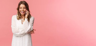 İletişim ve teknoloji kavramı. Beyaz elbiseli çekici beyaz kadın, sarışın kısa saç kesimi, akıllı telefonu tut, cep telefonuyla konuş ve gül, kaygısız gülümse, pembe arka plan