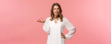 Whats your problem. Pissed-off and annoyed young blond girl looking questioned, cant understand what person complain about, raise on hand in dismay, shrug and grimace puzzled, pink background