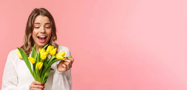 Frühling, Glück und Feiern. Porträt von überrascht und erfreut glücklich Mädchen fröhlich Blick auf Blumenstrauß, lächelt amüsiert, erhalten gelbe Tulpen, stehen rosa Hintergrund — Stockfoto