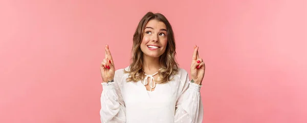 Retrato de primer plano de mujer atractiva optimista y esperanzadora en vestido blanco, labios mordidos y sonriendo como soñando despierto, sueño de esperanza hecho realidad, pidiendo deseos o rezando, de pie fondo rosa — Foto de Stock