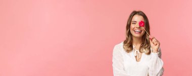 Bahar, mutluluk ve kutlama konsepti. Komik ve kaygısız genç sarışın kızın yakın plan portresi partilerde kız arkadaşlarıyla eğleniyor, dudaklarını tutuyor ve gülüyor, pembe arka plan