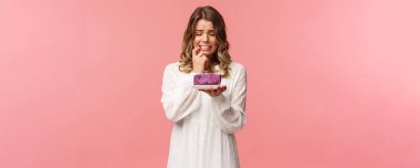 Tatiller, bahar ve parti konsepti. Tedirgin sarışın bir kızın portresi, dudak ısırması lezzetli pasta yeme arzusuna karşı koyamaz. Tereddütlü bir ifadeyle tatlıya bakar, endişeli suratını buruşturur.