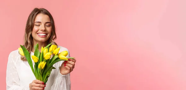 Frühling, Glück und Feiern. Nahaufnahme Porträt des schönen romantischen lächelnden Mädchens, das Blütenblatt der gelben Tulpe berührt, Blumen hält, Blumenstrauß auf Datum erhält, stehend rosa Hintergrund — Stockfoto