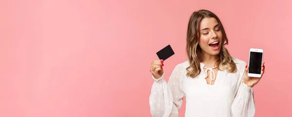 金融、购物和技术概念。身穿白衣的漂亮金发姑娘的特写，用智能手机在线购物更新她的春季衣橱，拿着信用卡 — 图库照片