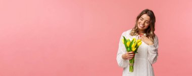 Tatiller, güzellik ve bahar konsepti. Mutlu, sevimli, romantik sarışın kızın portresi güzel bir buket çiçek alır, sarı lalelere bakar ve kalbe dokunur minnettar, gülümser.