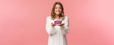 Tatiller, bahar ve parti konsepti. Doğum gününü kutlayan, mutlu doğum günü kızı portresi, dudak ısıran ve gülümseyen pasta üzerinde mum üflerken dilek tutan