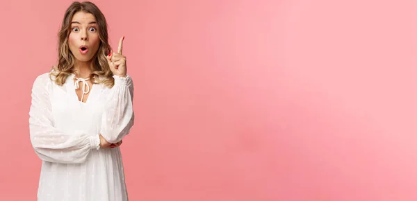 Belleza, moda y concepto de mujer. Retrato de chica rubia femenina sorprendida y excitada en vestido blanco, boca abierta jadeando divertido y levantar un dedo, tener sugerencia, solución encontrada — Foto de Stock