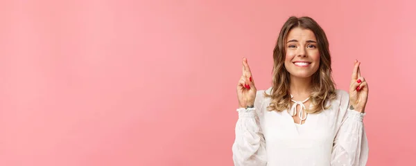 Retrato de cerca de la chica rubia hermosa esperanza pidiendo deseo, anticipando resultados importantes, dedos cruzados buena suerte y sonriendo como sentirse un poco nervioso, usar vestido blanco, fondo rosa — Foto de Stock