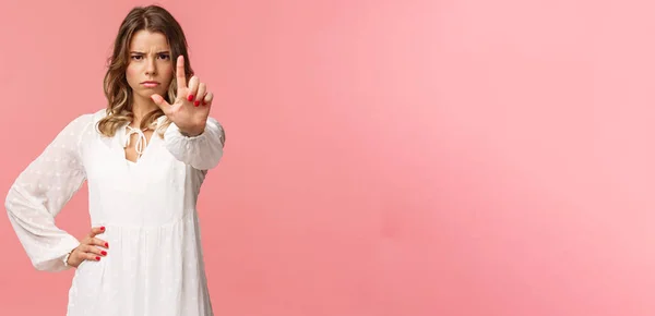 Basta, basta. Ritratto di ragazza bionda decisa e forte dall'aspetto serio in abito bianco, tendere la mano verso la fotocamera con un dito alzato in avvertimento, accigliato arrabbiato, proibire e proibire l'azione — Foto Stock