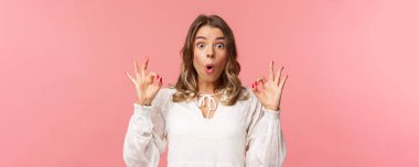 Nutku tutulmuş ve etkilenmiş, beyaz elbiseli güzel bir kızın yakın plan portresi. Gördüğü şey karşısında hayret verici bir performans. Dudaklarını kıvır, 