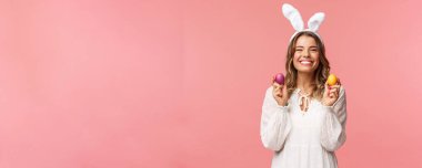 Tatiller, bahar ve parti konsepti. Sevimli, neşeli, tavşan kulaklı sarışın bir kızın portresi, elinde renkli yumurtalar, ailesiyle Paskalya kutlaması, yakın insanlarla geleneksel bir gün geçirmek.