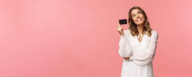 Parasını online alışverişe harcayacağını hayal eden sevimli, narin, sarışın bir kızın portresi. Hayalini kuran, teslimatı beklerken görüntüleyen, kredi kartı sahibi, pembe arka plan.