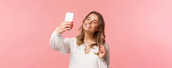 Close-up retrato de bela e elegante menina loira tirar selfie no parque na primavera, reunir gostos e seguidores, fazer conteúdo blogger, tirar fotos no smartphone, sorrindo fundo atrevida, rosa — Fotografia de Stock