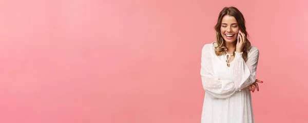 Технологическая концепция. Привлекательная белая женщина в белом платье, короткая стрижка, смартфон, разговор по мобильному телефону и смех, беззаботная улыбка, розовый фон — стоковое фото